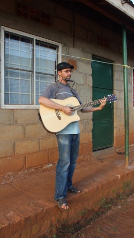 Shane Reichart playing guitar and harmonica in Uganda, Africa
